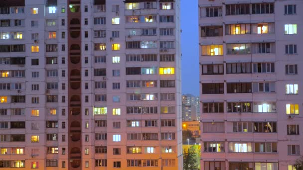Período nocturno de ventanas iluminadas del edificio por la noche con personas que viven en pisos con balcón. Concepto de consumo eléctrico. Vista desde abajo. Calle de la ciudad por la noche — Vídeo de stock