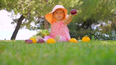 Mutlu çocukluk konsepti. Bebek için boş zaman etkinlikleri. Kız açık meyve ile oynuyor. Panama çocuk arka bahçede eğlenceli açık sahip. Toddler yeşil çim üzerinde anne bekliyor oturan