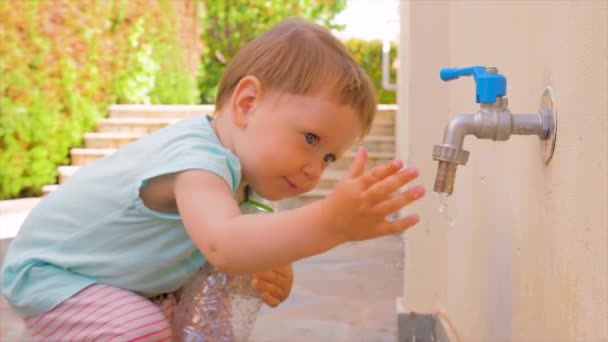 Küçük kız su ile oynuyor. Toddler su musluk akan ile oynuyor. Çocuğun yanında boş plastik şişe tutuyor. Su sorunları arka plan. Taze su problemleri. Anaokulu konsepti — Stok video