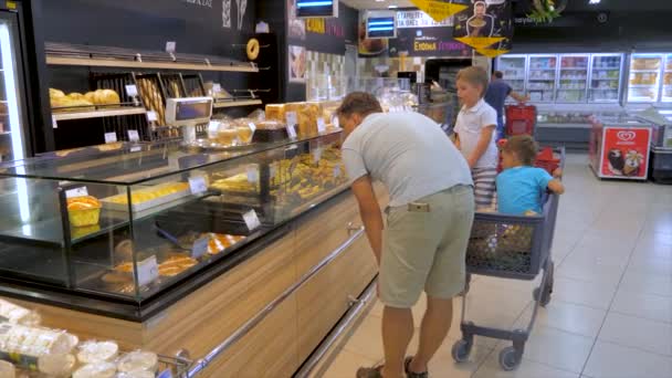 Döntéshozatal, amely termékek választani vásárolni. Apa vezetési fiai a bevásárlókosárban végig a szupermarketben. Örömteli szerető apa szórakozik a szupermarketben két aranyos kis fia — Stock videók