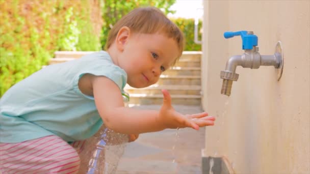 Kid håller tom plastflaska nära kran. Privat dagis bakgrund. Preschooler spelar på bakgård på sommaren. Montessori-konceptet. Leka med vatten. Taktila övningar på frisk luft — Stockvideo