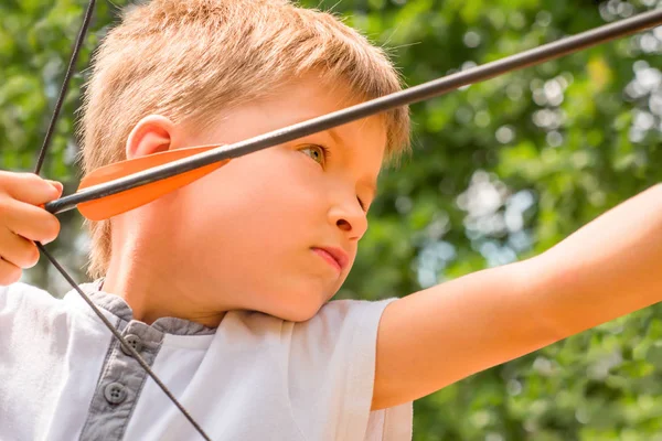 Chlapec s lukem a šípem na cíl. Kluk se díval na cíl. Dítě režie šipky na terč. Bowman pozadí. Děti a sport. Fyzický trénink. Alternativní školství — Stock fotografie