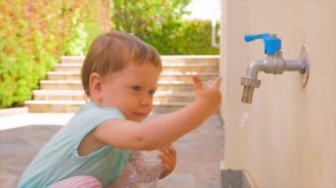 Küçük kız su ile oynuyor. Toddler su musluk akan ile oynuyor. Çocuğun yanında boş plastik şişe tutuyor. Su sorunları arka plan. Taze su problemleri. Anaokulu konsepti