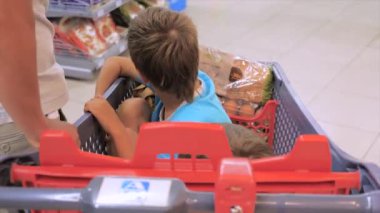 Baba, süpermarketboyunca alışveriş sepetinde oğullarını kullanıyor. Alışveriş arabasında oturan iki çocuk. Babalar içinde iki çocuk olan alışveriş arabasını kullanıyor. Süpermarket konsepti