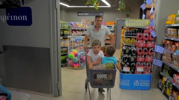 Shopping achtergrond. Kinderen zitten in de winkelwagen. Vader beweegt rond supermarkt met twee kinderen zitten in winkelwagen. — Stockvideo