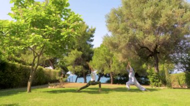 Yoga savaşçısı pozu yapan iki kadın. Yoga yaparak yaşlanma sürecini yavaşlatMak. Sağlıklı yaşam tarzı. Güçlü vücut konsepti. Mutluluk kavramı. Kızı açık vakit geçirmek ile Mutlu anne