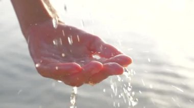 Kadın el seascape arka plan üzerinde içki su damlaları ile oynarken. Dişi, güneşte parlayan su damlalarıyla el sıkıştı. Deniz manzarası arka planda su damlaları ile kadın eli. Şehir dışı sahne