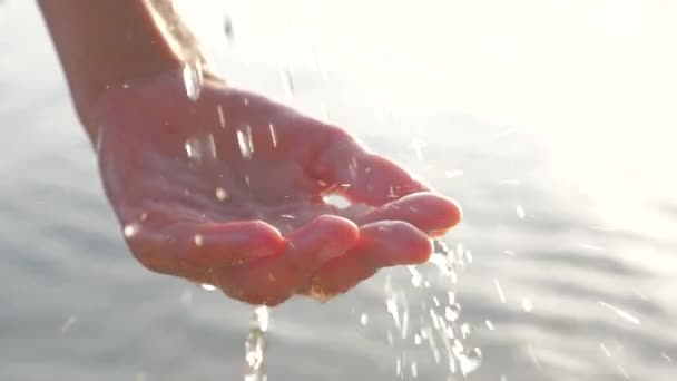 Женская рука играет с питьевой водой капли на морском фоне. Женская рука с капельками воды, сияющей на солнце. Женская рука с капельками воды на морском фоне. Загородная сцена — стоковое видео
