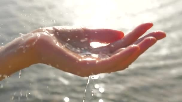 Mano de mujer jugando con gotas de agua de bebida en el fondo del paisaje marino. Mano acolchada femenina con gotas de agua brillando sobre el sol. Mano de mujer con gotas de agua sobre fondo marino. Escena no urbana — Vídeo de stock