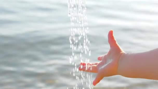 La mano del bebé captura gotas de agua en el fondo del paisaje marino. Mano del niño jugando con gotas de agua de bebida con agua de mar en el fondo. Niños y naturaleza. Concepto de agua potable — Vídeo de stock