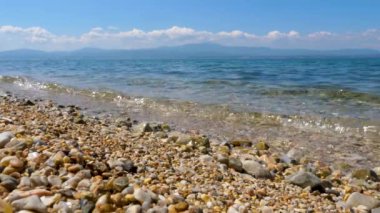 Arka planda deniz manzarası ve mavi gökyüzü ile Çakıl plaj. Sahilde mavi su ve çakıl ile Seascape arka plan. Güneşli yaz gününde sahil şeridi. Seyahat konsepti. Denizde tatil.