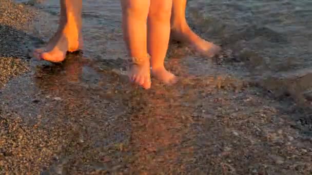 Тоддлер делает первые шаги на пляже. Малыш делает первые шаги с матерью на берегу моря — стоковое видео