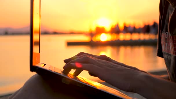 Hombre trabajando en un portátil cerca del mar. Varón con cuaderno sobre fondo de atardecer. Freelancer trabajando en la naturaleza. Antecedentes programadores. Antecedentes laborales distantes. Concepto de calidad de conexión a la red — Vídeo de stock