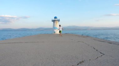 Young travelers playing with umberlla on pier near lighthouse. Europe travel with children. Family vacation background. Greece, island. Summer vacation children. Travel Eu