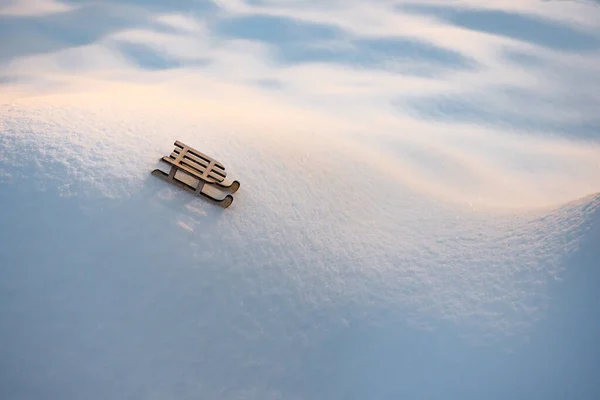 Παιχνίδι σε λευκό χιόνι. Έλκηθρο σε χιονισμένους λόφους και κοιλάδες. Παιδικό παιχνίδι από ξύλινο έλκηθρο σε φόντο χιονιού. Ευχετήρια κάρτα για τις χειμερινές διακοπές. Σύμβολο του νέου έτους. Ευχετήρια κάρτα, φυλλάδιο. Ιστορικό χιονιού — Φωτογραφία Αρχείου