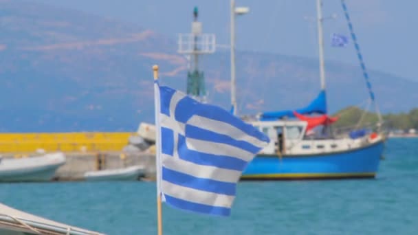 Bandiera greca con panoramica sul mare con barche e isola con montagna. Bandiera nazionale greca lusinghiero sul clima ventoso sul mare. Navi da pesca sullo sfondo con bandiera greca al centro dell'attenzione . — Video Stock