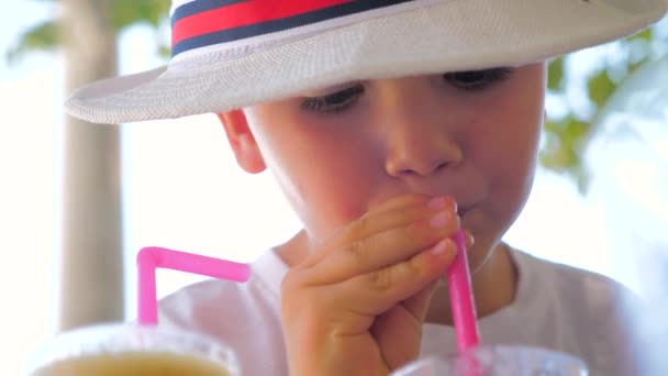 Напої для дітей, дітей. Хлопчик у капелюсі п'є коктейль на вулиці. Кафе дружнє до дітей. Щаслива концепція дитинства. Літній освіжаючий напій з льодом. Літні напої. Дитина п'є свіжий сік — стокове відео