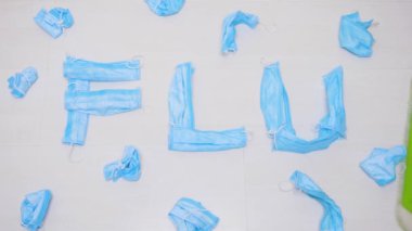 Kullanılmış tıbbi maskelerden yapılan FLU yazısını temizleyin. Grip kelimesinde katlanmış hijyenik maske kullanılmış. Paspasla silinmiş mavi tıbbi koruyucu maskeler. Salgın, salgın