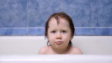 Ciddi küçük kız banyoda banyo yapıyor. Banyo yaparken kameraya bakan Avrupalı kızın yüzü. Çocuk banyo yapıyor. Banyoda suyla oynayan mutlu küçük kız. Banyodaki oyuncu çocuk.