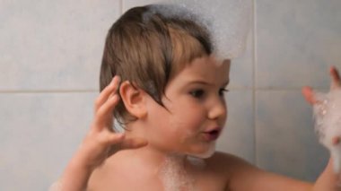 Çocuk banyo yaparken köpükle oynuyor. Yüz ifadesi. Kafasında köpük olan bir çocuk süper kahraman rolünü oynar. Montessori konsepti