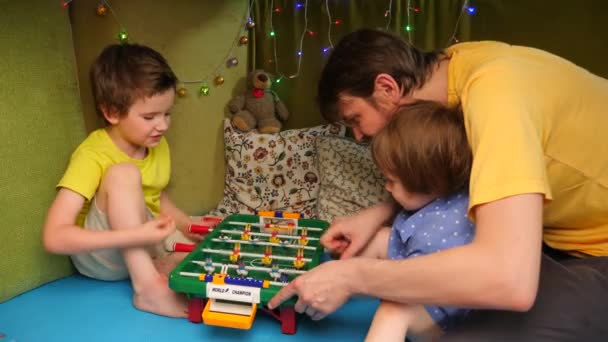 Apa gyerekekkel asztalifocizik a házban. A család otthon tölti az idejét. Vidám gyerekek játszanak apával a házban. Családi szabadidős tevékenység. Karantén, boldog család. — Stock videók