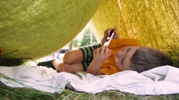 Trekking Pequeña casa para niños. Niño con teléfono, móvil jugando videojuegos. Niño pasar el tiempo de verano en la tienda con aplicaciones móviles . — Vídeos de Stock