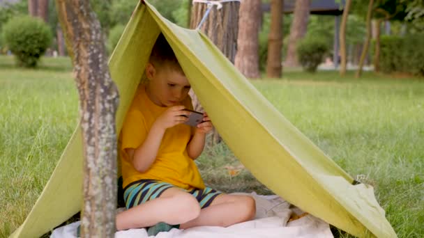 Jovem viajante em tenda jogar videogame. Conceito de viagem. Boy in hand made jogo de barracas no celular. Criança na natureza com gadget . — Vídeo de Stock