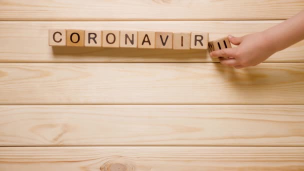 Děti ručně tvoří koronavirové slovo z dřevěných bloků. Dřevěné pozadí. Dřevěná hračka. Globální šíření infekce. Nebezpečný virus. Ruka dítěte stavět koronavirové slovo z kostek. Dětská hra — Stock video