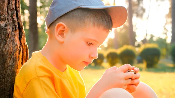 儿童在户外流动阅读电子书 小孩带着小玩意在公园花园戴帽子的男孩在智能手机上玩游戏 电子学习 在线教育 学龄前儿童花时间在新鲜空气上 心理学 — 图库照片