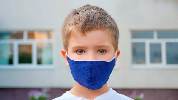 Un masque de touriste. Un garçon caucasien face portant un masque médical de retour à l'école dans le fond de la ville. Un garçon beaux yeux. Les yeux des enfants. Jeune touriste, petit voyageur en masque facial — Photo