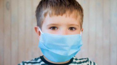 Tıbbi maskeli bir çocuk kameraya bakıyor. Coronavirus, covid-19 salgını. Maskeli 6 yaşındaki çocuğun kahverengi gözleri. Virüs, bakteri, salgın hastalık. Koronavirüsten korunmak için sağlık kuralları