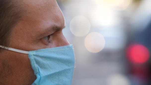 Şehir caddesinde tek kullanımlık tıbbi maske takan bir gencin profili. Maskeli adam bulanık arkaplanda kameraya bakıyor. Caddedeki virüs maskesi Coronavirus önleme covid-19 için korunuyor — Stok video