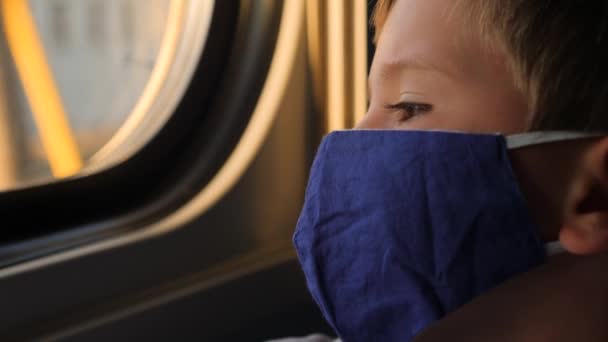 Giovane maschio con maschera facciale guardando il finestrino del treno. Ragazzo di sei anni in maschera protettiva viaggia in treno. In quarantena e in viaggio. Ritorno a scuola dalle vacanze. Torniamo a scuola. Ritorno dalle vacanze — Video Stock