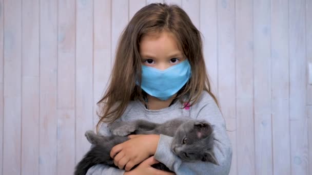 A vida durante uma pandemia de coronavírus. Escola durante a quarentena. Regiões da Zona Vermelha. Menina com um gatinho em uma máscara descartável médica. Usar uma máscara facial. Prevenção e controle de infecções de PCI — Vídeo de Stock