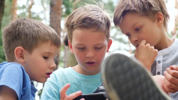 技術と教育の概念 若い男の子 スマートフォンと兄弟の友人 3人の男の子が屋外でビデオゲームをプレイ 子供時代とItの概念 — ストック動画