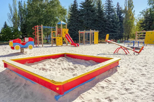 Parkta renkli çocuklar için oyun parkı ayarlandı. Ön planda kum havuzu. Çocuksuz oyun alanı seti. Oyun sahası, kum havuzu, denge ve diğer oyun alanı elemanları. Açık hava çocuk parkı. Kumlu toprak