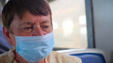 Yorgun, yaşlı bir kadın maske takıyor, koruyucu maske takıyor. Toplu taşımada tek kullanımlık mavi tıbbi maske takmak. Solunum hastalıkları koruması. Coronavirüs salgınına sosyal mesafe