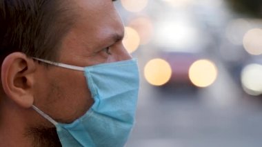 Şehir caddesinde tek kullanımlık tıbbi maske takan bir gencin profili. Bulanık arka planda koruyucu maskeli adam kalabalık bir şehirde. Yüz maskeli insanlar. Coronavirüs önleme için yüz maskesi covid-19