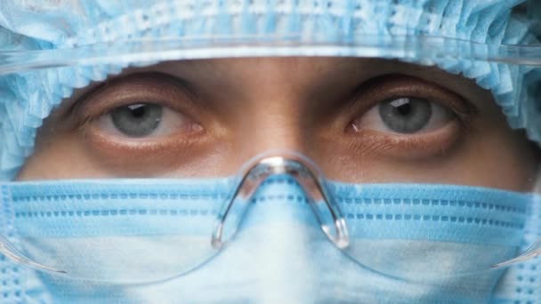 Orvosnő biztonsági egyenruhát és orvosi védőszemüveget visel. Kutatólaboráns. Női orvos közeli portréja Coronavirus-járvány idején Covid-19, Novel Coronavirus 2019-nCoV — Stock videók