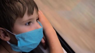 Tren yolculuğu sırasında pencereden içeri bakan düşünceli bir çocuk. Tecritten evine dönen, maskeli bir çocuğun yüzü. COVID-19, koronavirüs. Facebook maskeli çocuk Expres 'ten Pencerede İzliyor