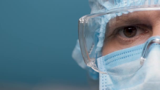 Εργαστήρι Προσωρινής Προστασίας Εργαζομένων και γυαλιών. Εστιασμένα μάτια γιατρών που κοιτάζουν την κάμερα. Μισόφατσα. Νοσοκομειακός εργάτης άντρας σε ιατρικό κιτ και προστατευτικά γυαλιά από κοντά. Covid-19 — Αρχείο Βίντεο