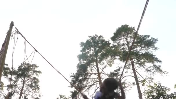 Malý dětský skok na trampolíně s elastickými provazy. Šťastný chlapec letí na oblohu. Malá silueta skákající na trampolíně Bungee Jumping. Kluk v bezpečnostním pásu skáče vysoko. Dětské vzpomínky — Stock video