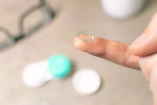 contact eye lens on the finger. glasses and container are blurre