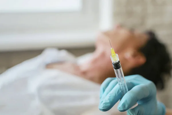 一把注射器放在美容师的手里 病人躺在背景模糊 — 图库照片