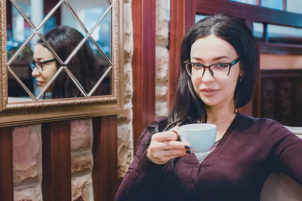 Vackra brunett tjej med en kopp kaffe sitter bredvid en spegel — Stockfoto