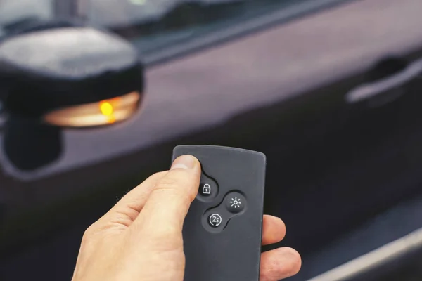 key card. finger presses the button to open the car. the car on the background is blurred