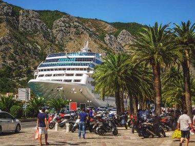 Liner arasında dağlar ve palmiye ağaçları, limanda bir iskele insanlar ve taşıma