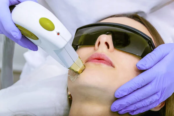 A woman performs a photo rejuvenation cosmetological procedure. Photo therapy for the face. Anti-aging procedures