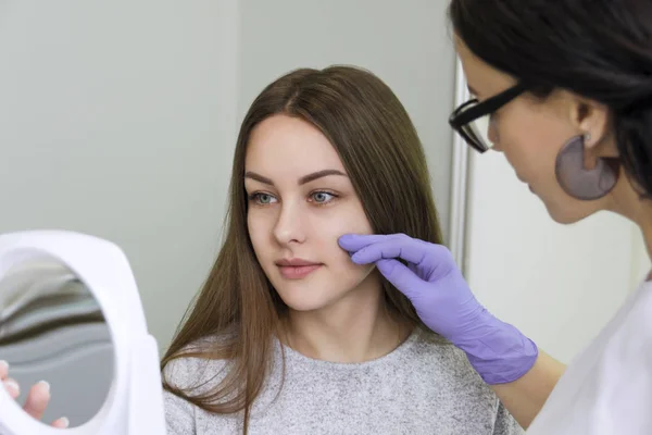 Female cosmetologist showing to young pretty woman the face zones to apply clinic treatment. Medicine, aesthetic and beauty concept