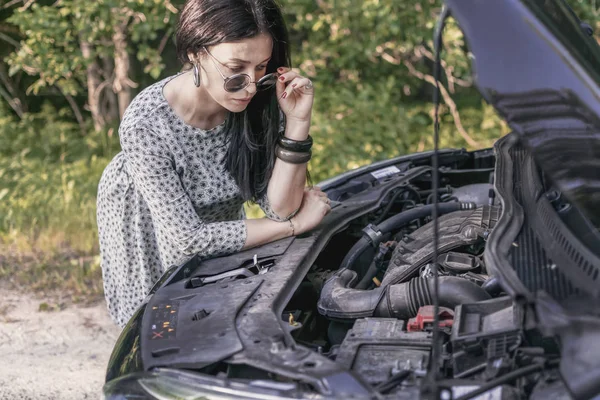 üzgün çekici kadın şehir dışında kırık bir arabanın kaputunun altında görünüyor
